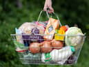 A woman holds a shopping basket of groceries.