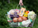 A woman holds a shopping basket of groceries.