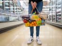 A woman holds a basket of goods in a supermarket.