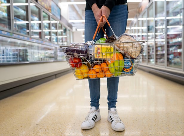 <p>A woman holds a basket of goods in a supermarket.</p>