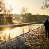 A man walks on the snow-covered path by the New River at sunrise, as steam rises from nearby houses in London.