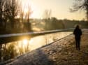 A man walks on the snow-covered path by the New River at sunrise, as steam rises from nearby houses in London.