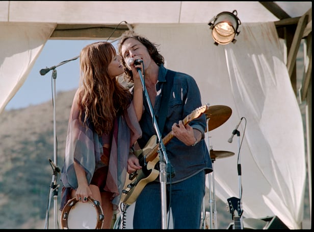 <p>Riley Keough as Daisy Jones and Sam Claflin as Billy Dunne in Daisy Jones & The Six, singing into a shared microphone (Credit: Lacey Terrell/Prime Video)</p>