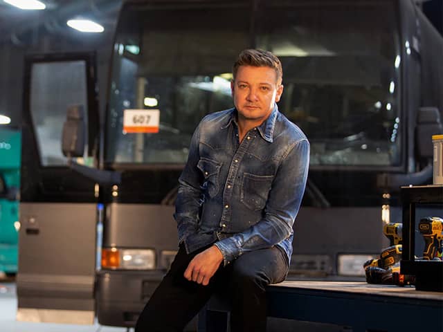 Jeremy Renner on set of Rennervations, a bus behind him and some power tools to one side (Credit: Disney+)