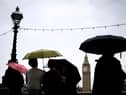 Pedestrian stand under umbrellas while looking at Elizabeth Tower, commonly called Big Ben from the Southbank by the River Thames, in central London, on July 31, 2023 on a gloomy and rainy summer day.