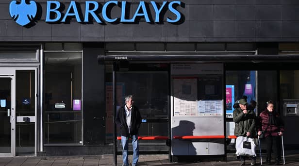 Commuters wait at a bus stop outside a branch of Barclays in London.