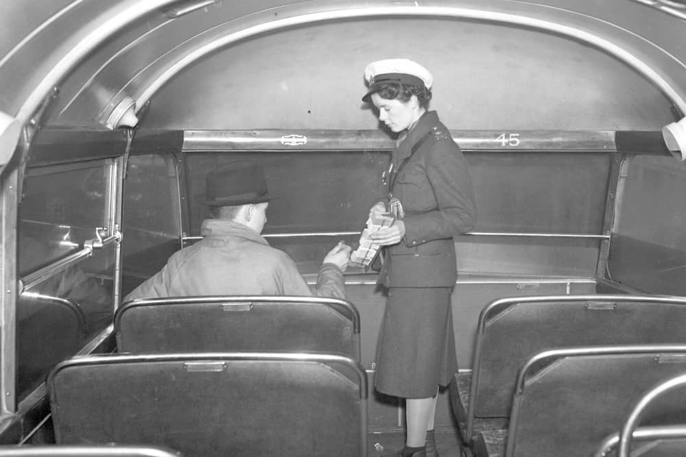 A bus conductress collecting fares from a passenger.