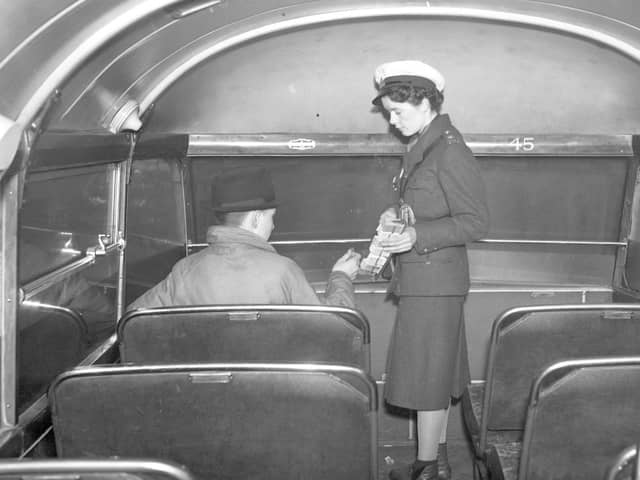A bus conductress collecting fares from a passenger.
