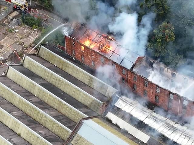 Flames and smoke pour from roof of factory building.