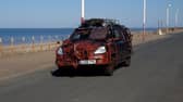 A zombie themed vehicle driving on a road by the coast