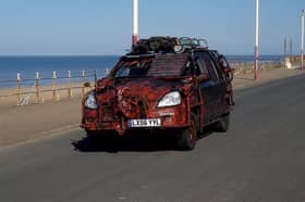A zombie themed vehicle driving on a road by the coast