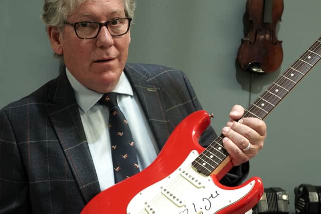 Auctioneer Nigel Smith pictured holding the signed Mark Knopfler guitar.
