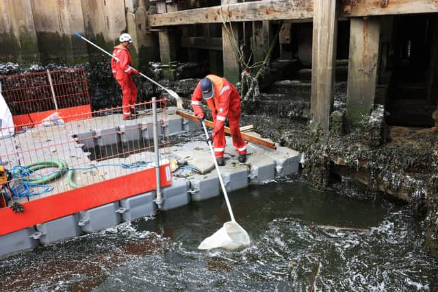 Workers on floating pontoon platforms using nets to capture pellets in the river Tyne