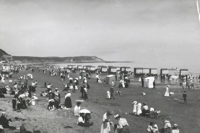 Crowds on the beach at Scarborough, North Yorkshire, with a row of bathing machines at the water's edge, 1890s.