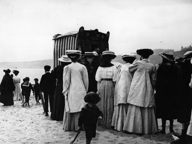 June 1908: Crowds gather to watch a Punch and Judy puppet show on the beach at Scarborough.