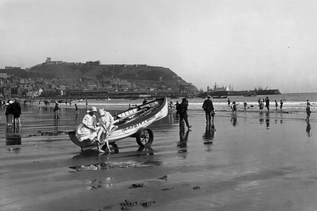 31st August 1923: Holidaymakers on the sands at Scarborough, Yorkshire. The town lies on the hill in the background. Two girls sit on a rescue boat drawn up on the sand.