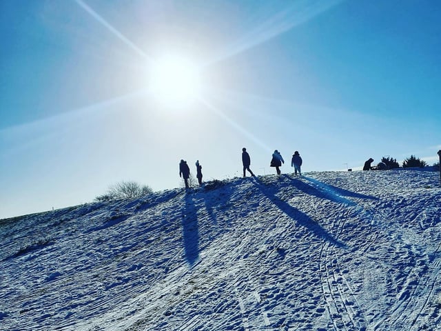 The winter sun casting silhouettes on a snowy hill, covered with the tracks of sledges.
