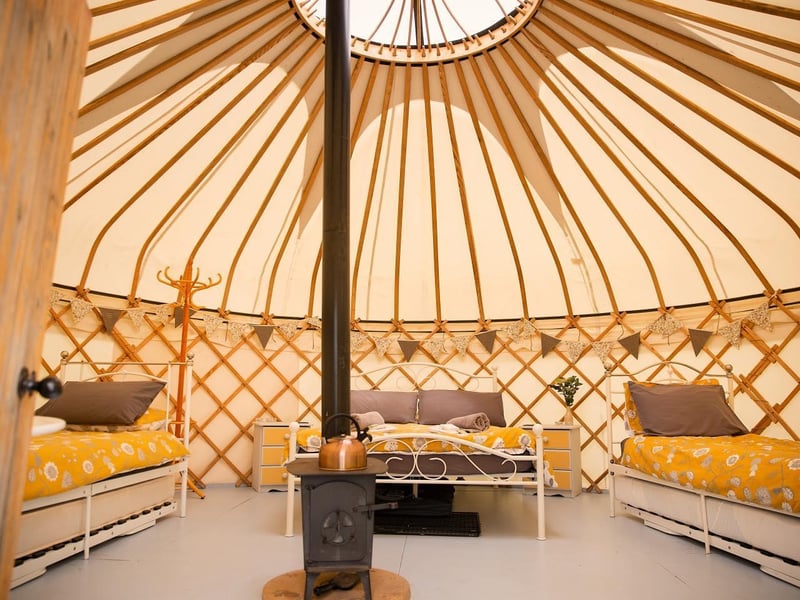 Country Bumpkin Yurts is all about escaping the everyday and embracing nature. Yurts are beautiful structures filled with home comforts, whilst also keeping their camping vibes and element of adventure. They are the best of both worlds.
This site comprises three traditionally designed yurts with private bathrooms and alfresco kitchens. Two of the yurts can sleep up to six people and the smaller yurt accommodates two. A log burner, shabby chic furnishings and cosy beds are in each tent, so you can rest in comfort and style. An eco-friendly wood burning hot tub makes it a yurt glamping experience for those looking for an extra special stay. Based on Waterloo Cottage Farm in the small village of Great Oxendon, Country Bumpkin Yurts provides an immersive countryside experience with bridleways, great walking, cycling, leisure and eating out opportunities just a stones-throw away.