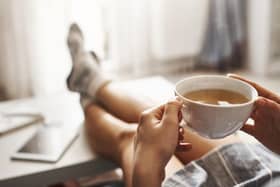 Cup of tea and chill. Woman lying on couch, holding legs on coffee table, drinking hot coffee and enjoying morning, being in dreamy and relaxed mood. Girl in oversized shirt takes break at home.