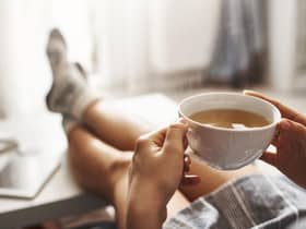 Cup of tea and chill. Woman lying on couch, holding legs on coffee table, drinking hot coffee and enjoying morning, being in dreamy and relaxed mood. Girl in oversized shirt takes break at home.