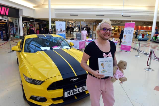 Richie Smith alongside his Mustang sports car and holding his book "The Art of Weeing In The Sink".