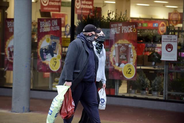 Passersby wearing face coverings, which will soon be no longer required in shops.