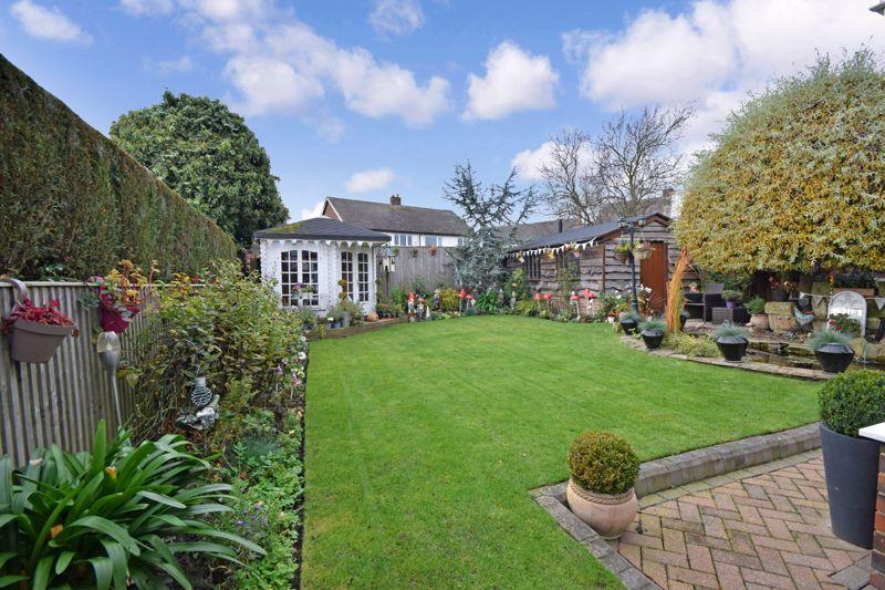 Good-sized rear garden with a patio and lawn, white summerhouse with timber decking.