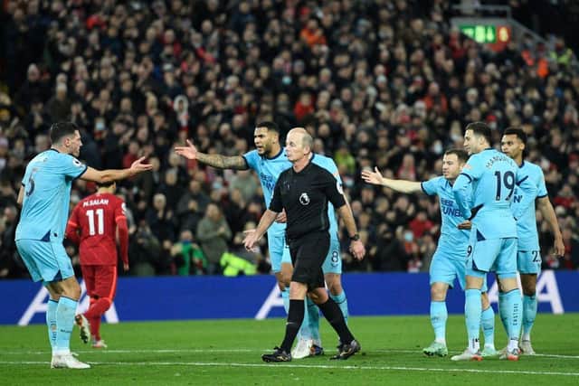 English referee Mike Dean (C) walks away from Newcastle players after they concede their first goal during the English Premier League football match between Liverpool and Newcastle United at Anfield in Liverpool, north west England on December 16, 2021. (Photo by OLI SCARFF/AFP via Getty Images)