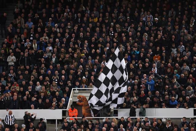 A Newcastle United fan, wearing an inflatable T-Rex costume, waves a large White and Black chequered flag during the Premier League match between Newcastle United and Everton FC at St. James Park on October 19, 2022 in Newcastle upon Tyne, England. (Photo by George Wood/Getty Images)