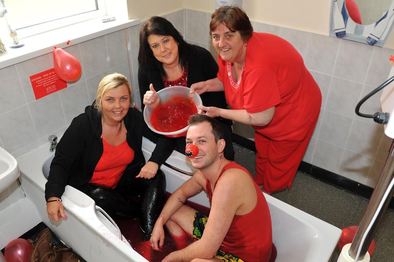 Warrior Park Care Home staff Laura Tomkins and Liam Wood sat in a bath of red jelly for charity 8 years ago. Making sure it was topped up were fellow staff members Susan Farnsworth (left) and Jan Teasdale.