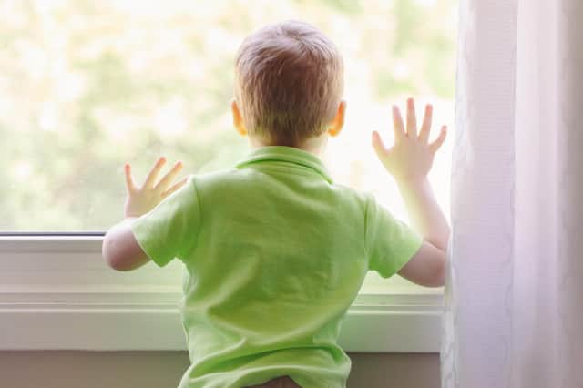 A boy at home looking out the window, waiting for someone to come home.