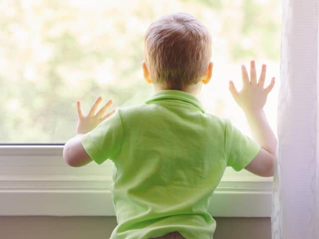A boy at home looking out the window, waiting for someone to come home.