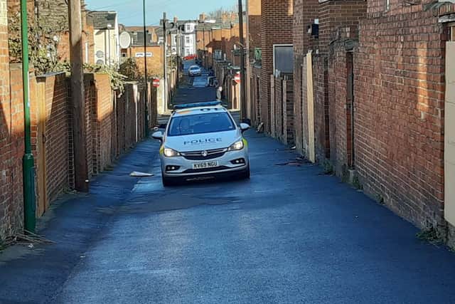 A police vehicle remains on duty in the back lane behind the street.