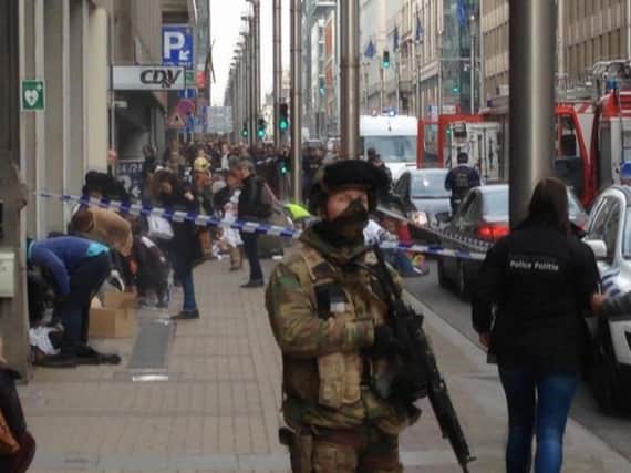 In this image taken from TV, an armed member of the security forces stands guard as emergency services attend the scene after a explosion in a main metro station in Brussels.