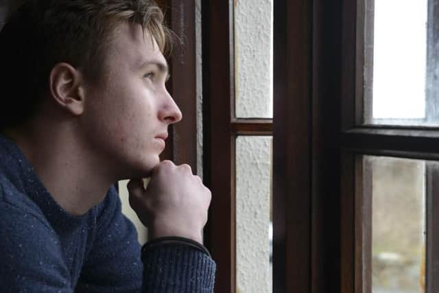 A young man suffering from depression looks out a window wondering how to cope with the day ahead.