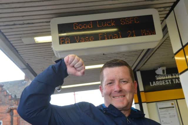 Supporter Colin Browne in front of the good luck message for South Shields FC displayed at South Shields Metro Station.